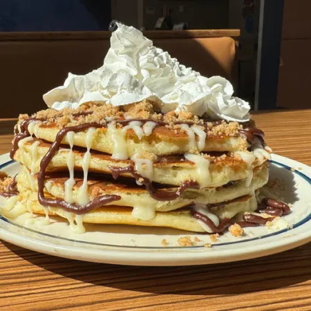 stack of 4 pancakes drizzled with chocolate icing, brown sugar and topped with whipped cream