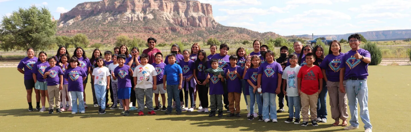 40 students and staff are wearing purple ZYEP shirts posing in a line for a group picture with the Dowa Yalanne mesa in the background