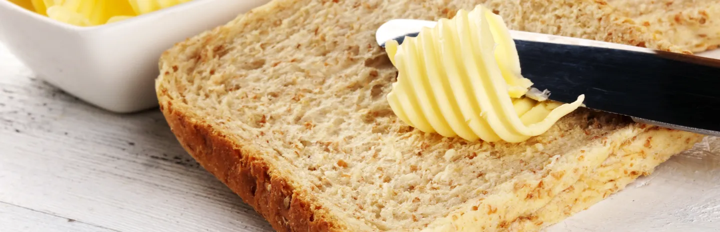 closeup of a butter knife spreading buttery spread on multigrain bread