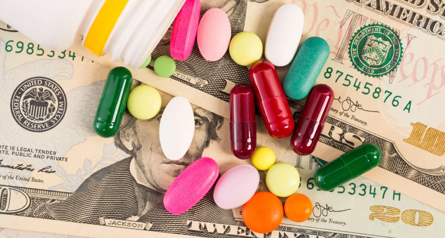 Money with a handful of supplements and tablets on top.