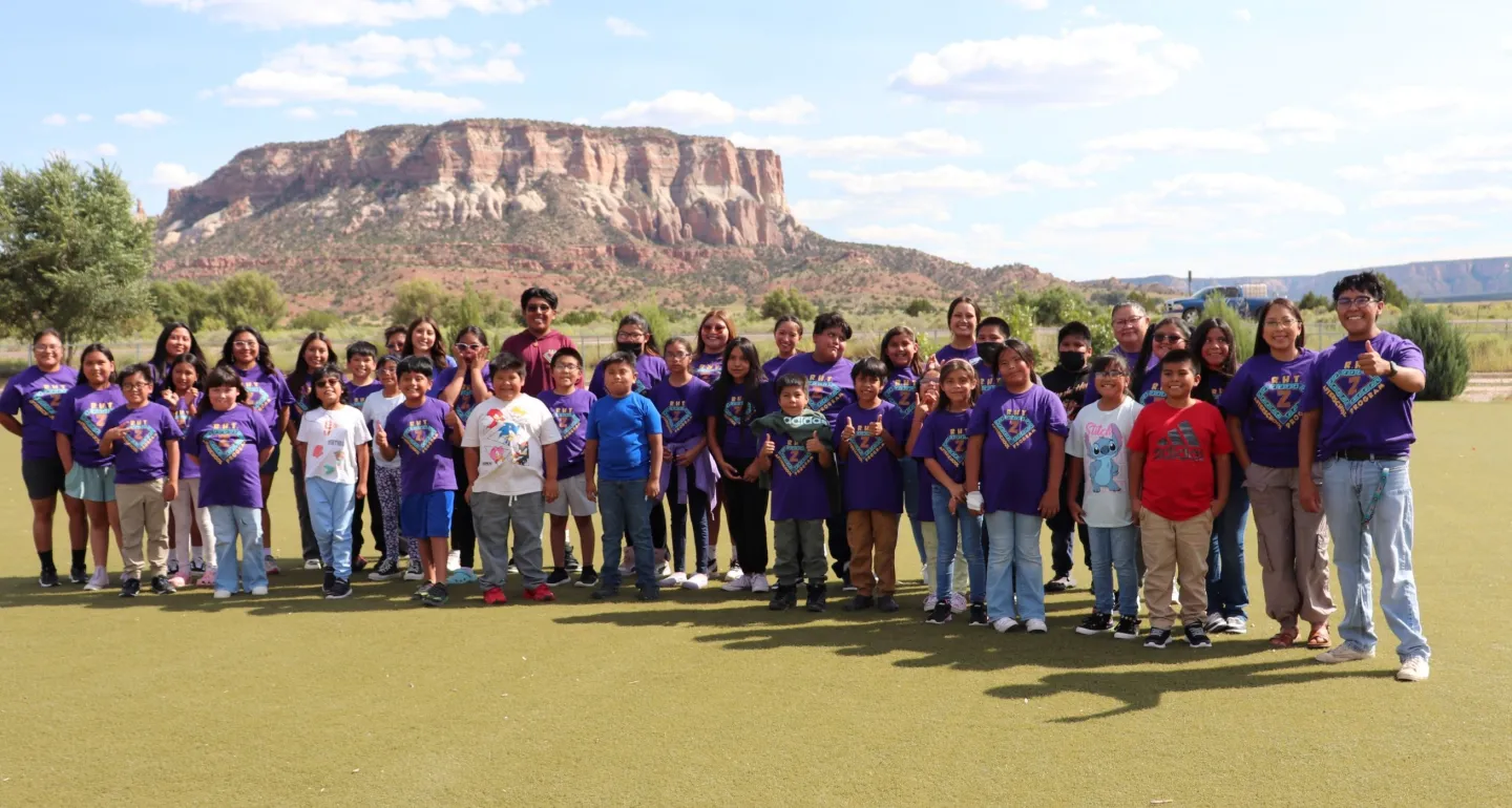 40 students and staff are wearing purple ZYEP shirts posing in a line for a group picture with the Dowa Yalanne mesa in the background