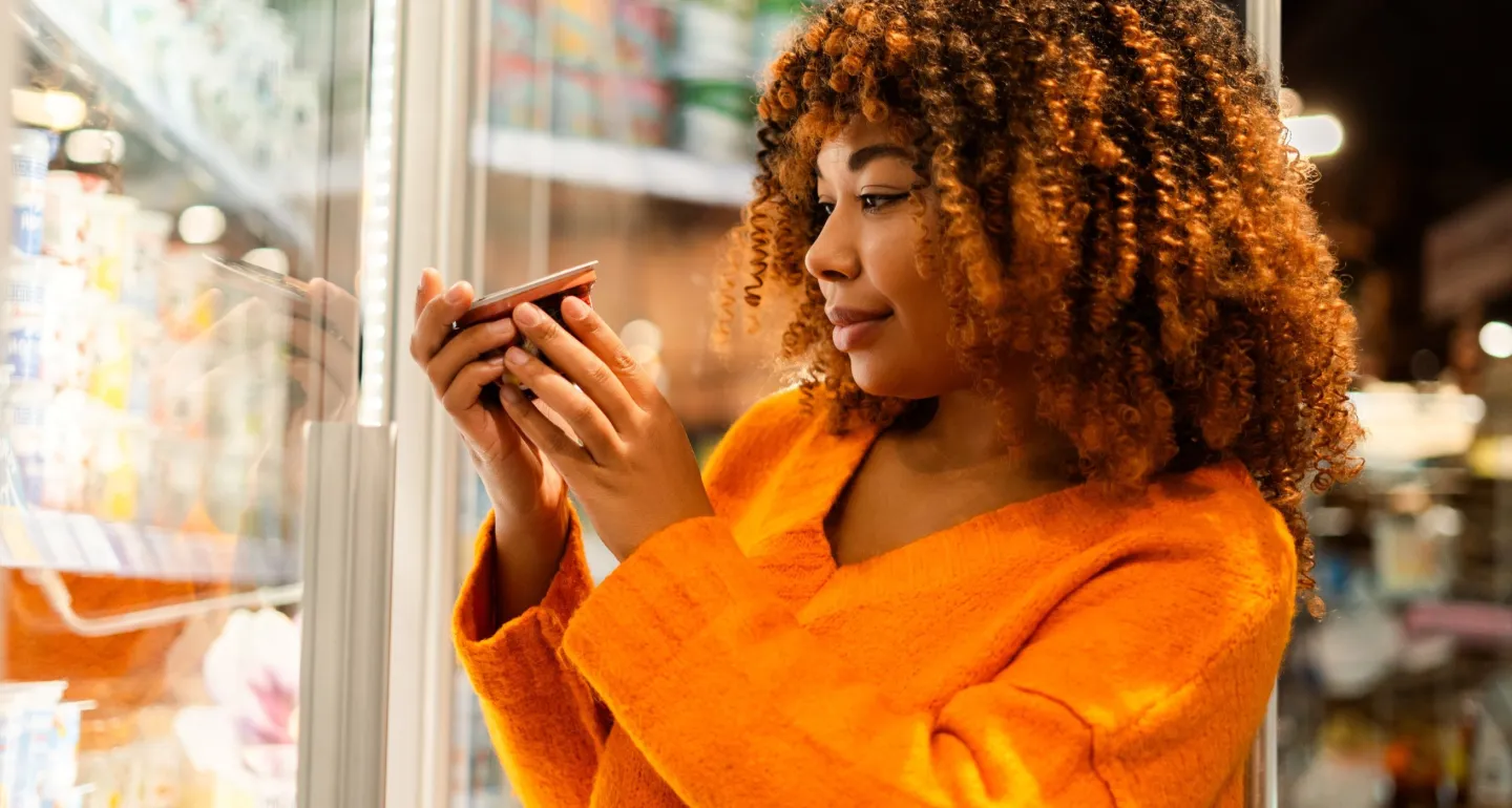 A woman reads the labels of a refrigerated product at the grocery store