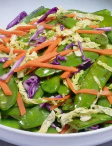 Plate with stir-fried snow peas, shredded carrots and cabbage