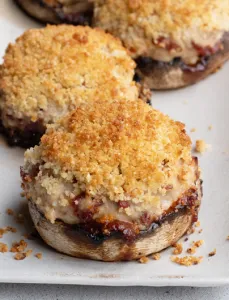 white plate with 2 stuffed Portobello mushrooms topped with breadcrumbs