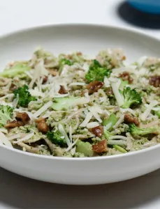 white bowl filled with pesto pasta and walnuts