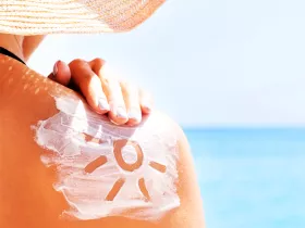 person rubbing sunscreen on their shoulder on a sunny day.