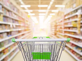 Supermarket aisle product shelves interior blur background with empty shopping cart