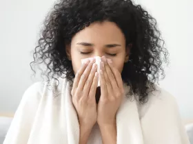 woman with blanket around her shoulders blowing her nose