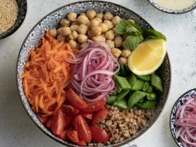 bowl filled with un-mixed vegetables like shredded carrots, red onion, chickpeas, and more