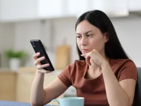 Woman looks skeptically at phone in kitchen