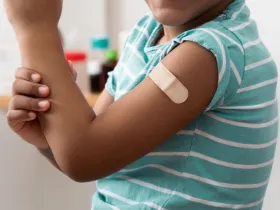 A Black child shows off their arm with a bandage over a vaccine injection site