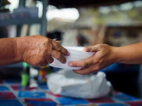 Closeup of a person handing a bowl of food to another person.