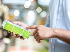 A man in a blue shirt is holding a green box and pointing at the details printed on it while shopping.