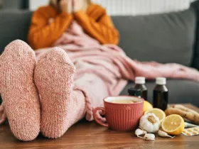 Feet wearing warm socks on a low table beside cold medicine and home remedies