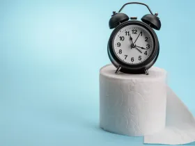 alarm clock sitting on a roll of toilet papper