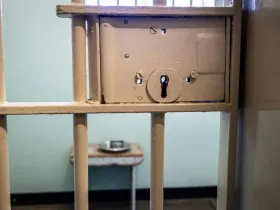 A locked prison cell with a metal food container inside.