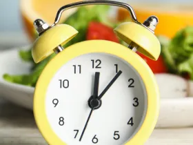 old yellow alarm clock in front of a plate of salad