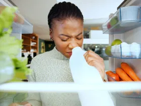 woman sniffing milk carton inside a fridge