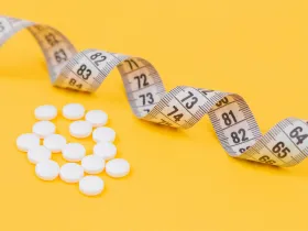 A measuring tape and weight loss pills on a yellow background