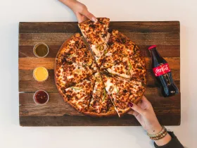 Overhead view of a pizza and bottle of soda on a cutting board