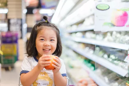 Girl holding an apple in grocery store