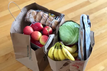 Two paper grocery bags full of apples, bananas, cabbage, and bread products