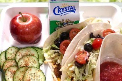 A lunch tray: tofu tacos, cucumber salad, an apple, and milk.