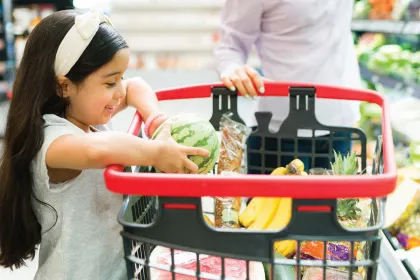 Young girl placing produce into a shopping cart