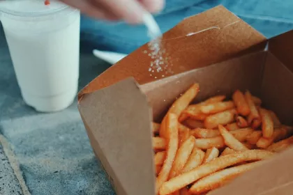 A person sprinkling extra salt on their fast food fries