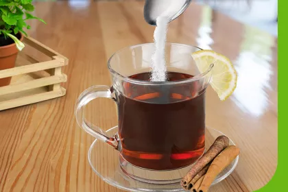 clear mug holding tea pouring sugar into