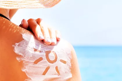 person rubbing sunscreen on their shoulder on a sunny day.