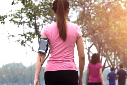 woman in a pink shirt walking away fromthe camera and waring a phone holder on her arm