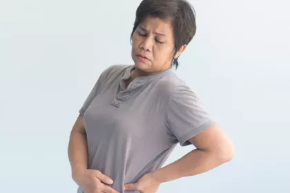 woman in grey shirt holding her hip and wincing in pain