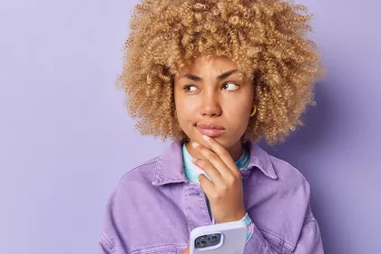 person in purple shirt with purple background holding a phone and holding their chin