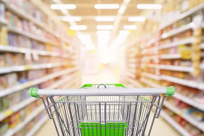 Supermarket aisle product shelves interior blur background with empty shopping cart