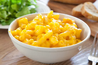 Bowl of macaroni and cheese with bread and salad in background