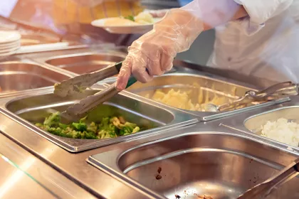 Chef standing behind full lunch service station with assortment of food in trays.
