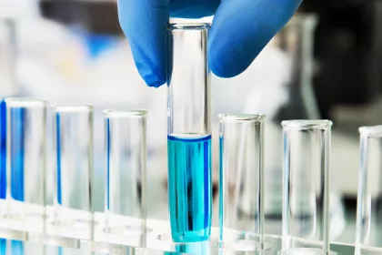 row test tubes one being held by a hand with gloves contains blue liquid