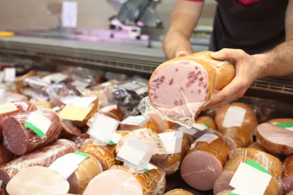 Male seller holding piece of deli meat in butcher shop