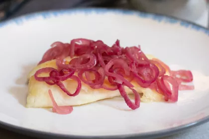 tilapia on a plate covered in cooked red onions