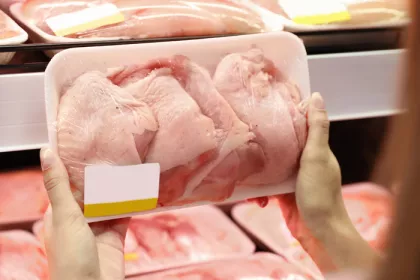 person holding a package or raw chicken in front chicken shelf at supermarket