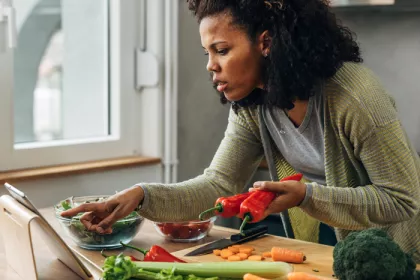 woman checking ipad while cutting vegetables in kitchen