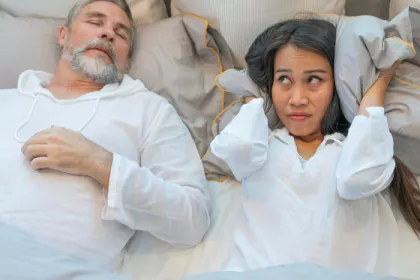 one person sleeping soundly and the person next to them shielding their ears with a pillow
