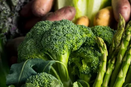Seasonal produce - a closeup of broccoli and asparagus in the foreground, with potatoes, cabbage, collard greens and kale in the background.