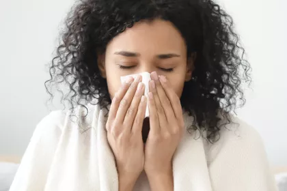 woman with blanket around her shoulders blowing her nose