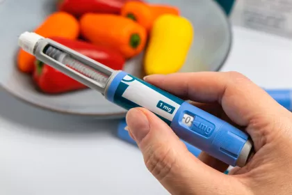 hand holding an obesity medication applicator with bell peppers in the background