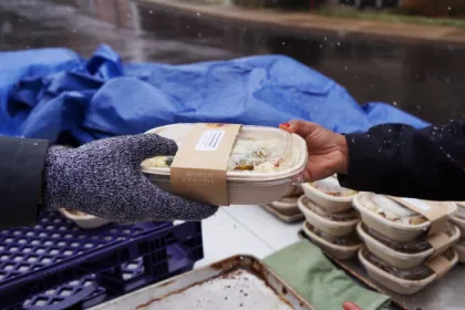 A Make Food Not Waste worker hands a recipient a meal