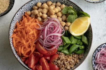 bowl filled with un-mixed vegetables like shredded carrots, red onion, chickpeas, and more