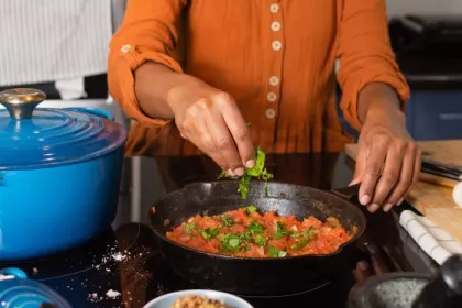 A woman in an orange shirt tears basil over a pot of tomato sauce