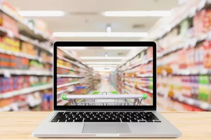 Laptop computer on wood table with supermarket aisle blurred background online shopping